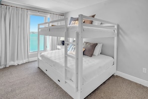 Un lit superposé avec vue sur la mer, une table de chevet avec une lampe et une fenêtre avec des rideaux.