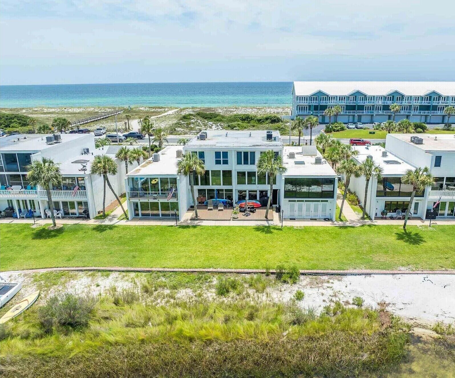 A beachfront hotel with multiple buildings, a parking area, and a view of the ocean.