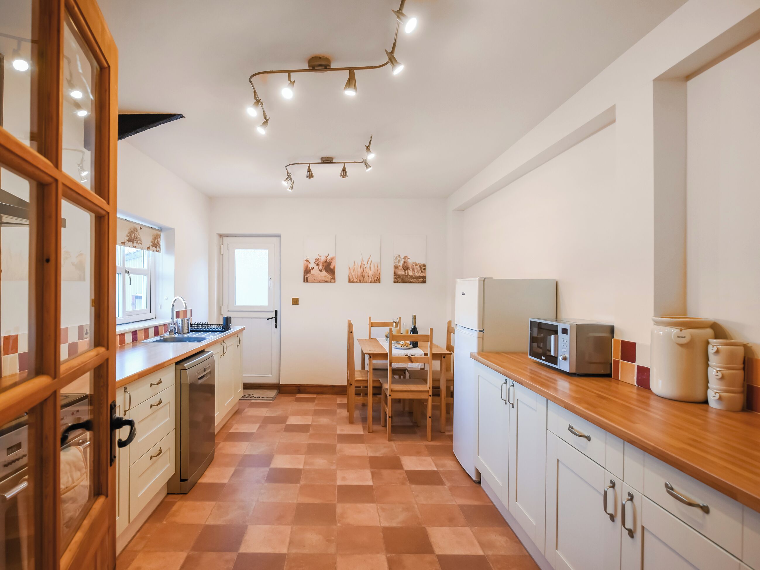 A compact kitchen with a wooden countertop, a sink, a refrigerator, a microwave, and a dining area with a table and chairs.