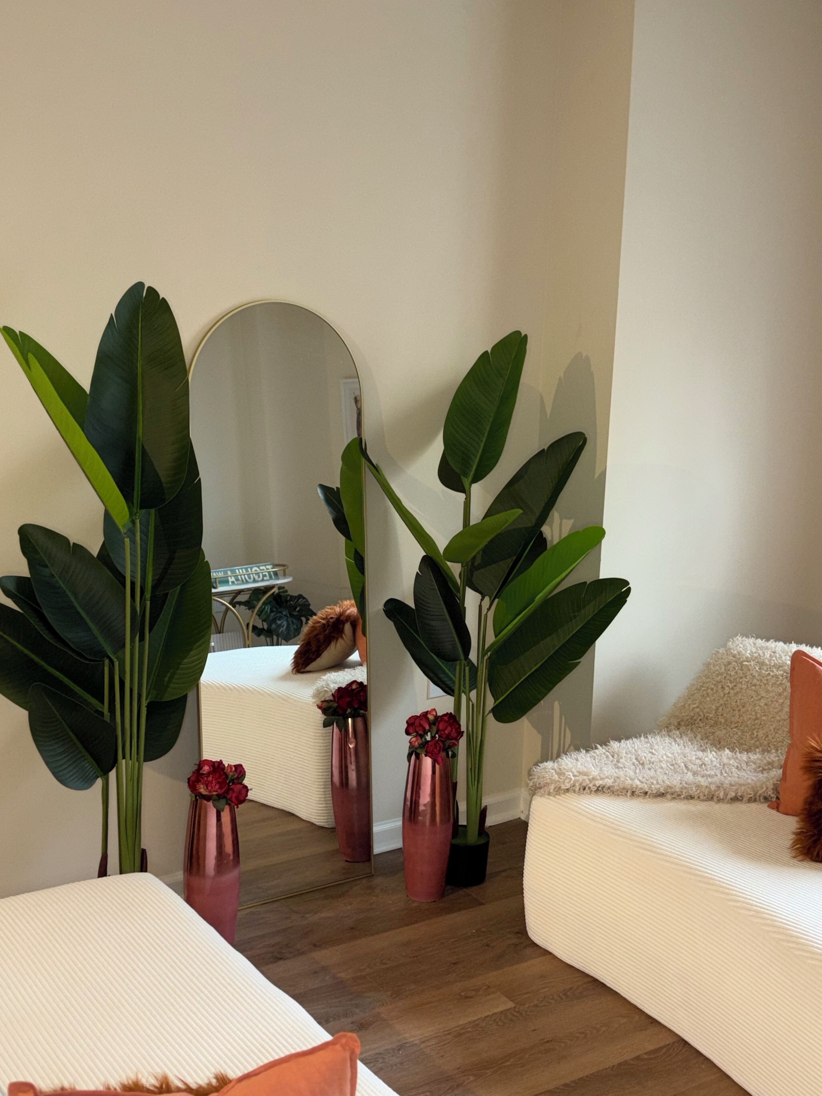 Een moderne woonkamer met een grote spiegel, een witte bank en verschillende potplanten.