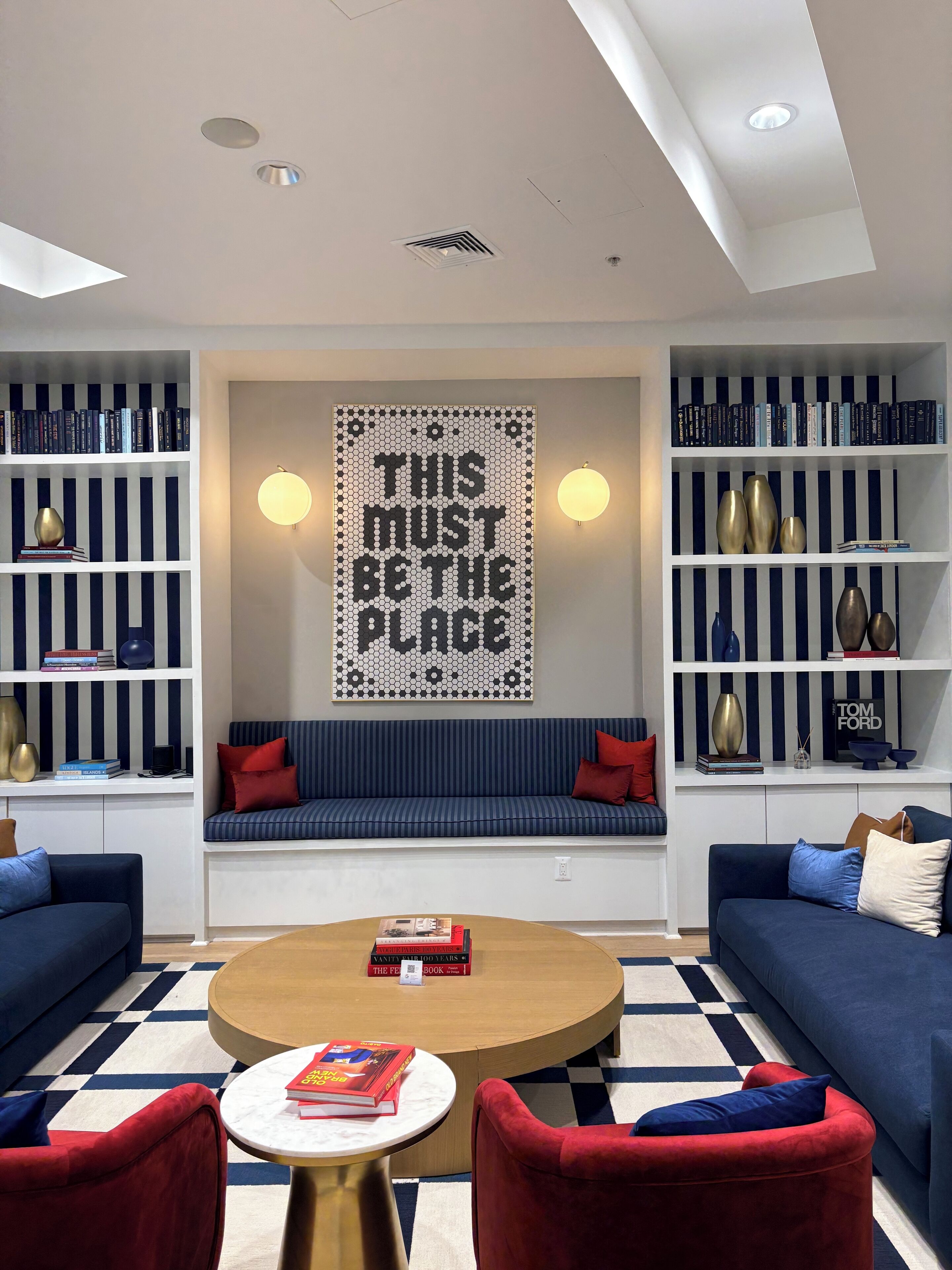 A modern living room with a central seating area, bookshelves, and a decorative wall piece.