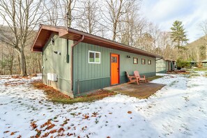 A single-story building with a green exterior and a red door, surrounded by trees and snow.