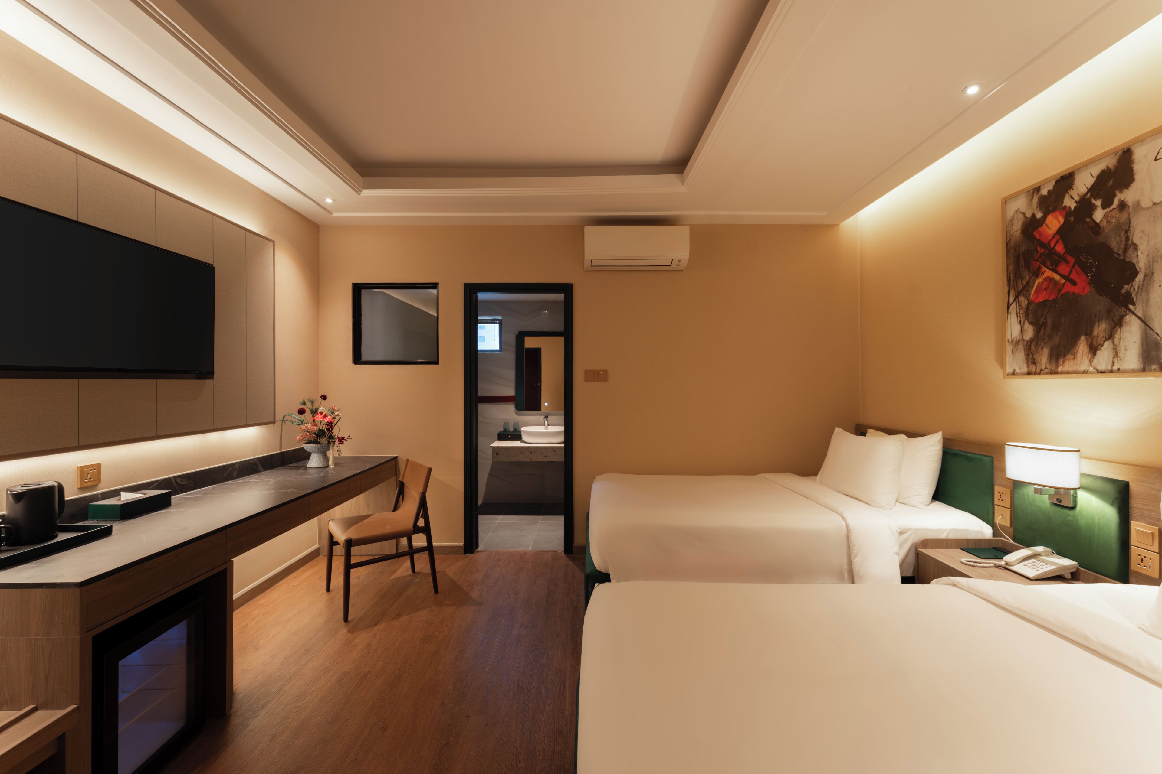 Quarto de hotel com televisão de tela plana, escrivaninha com cafeteira, duas camas, uma cadeira e um quadro na parede.