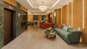 A modern hotel lobby with a green sofa, a red reception desk, and a chandelier. - NiK Hotel Thi Sach (Ho Chi Minh City)