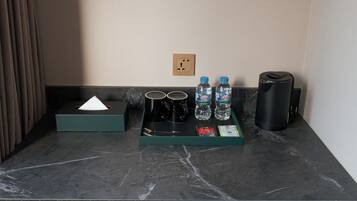 A hotel room's minibar with a tissue box, two black mugs, two LaVie water bottles, a black thermos, and a tray with a spoon and napkin.