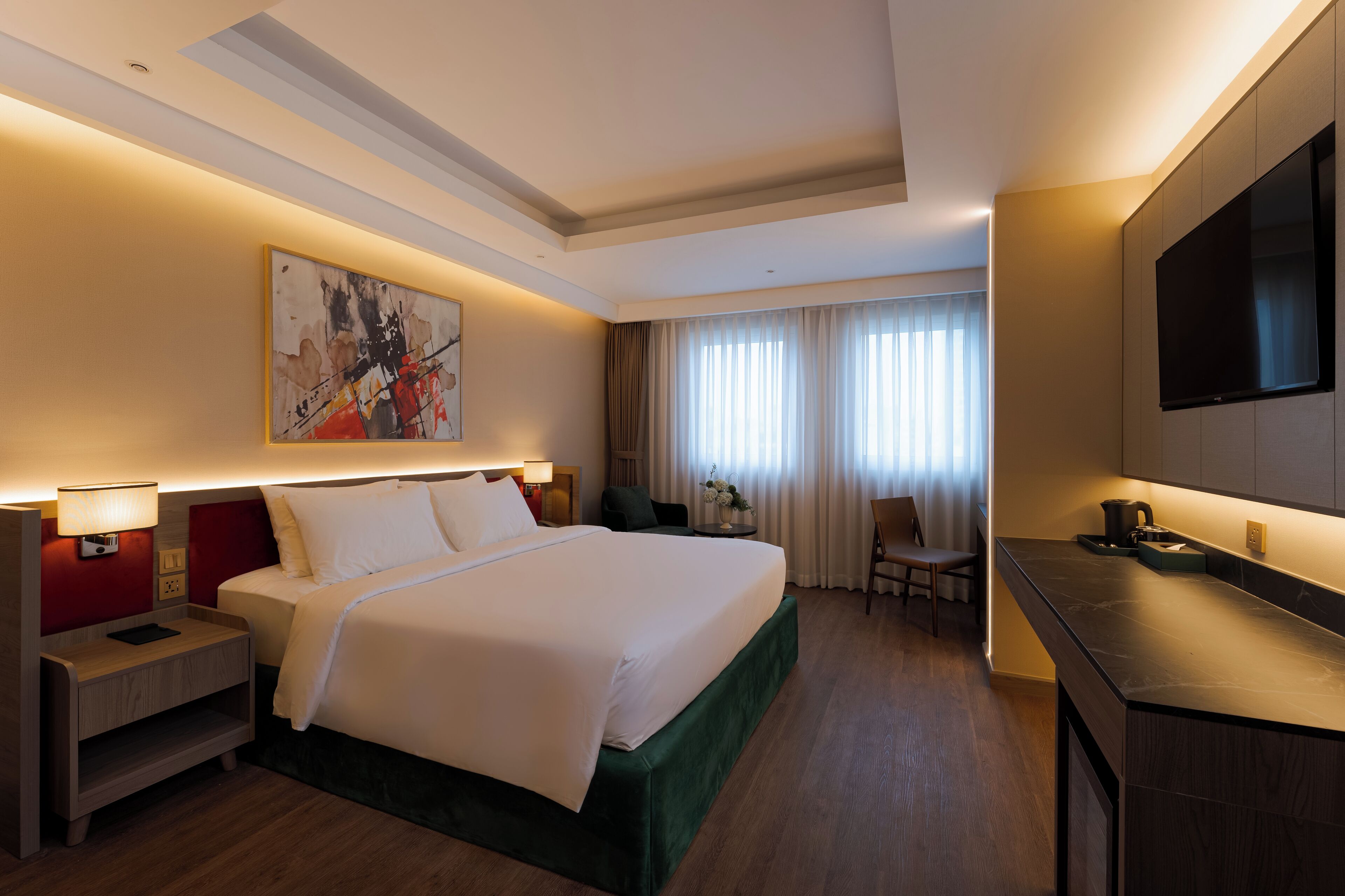 Ein Hotelzimmer mit einem großen Bett, Nachttischen, einem Schreibtisch, einem Sessel und einem Fernseher, sowie einem Fenster mit Vorhängen.