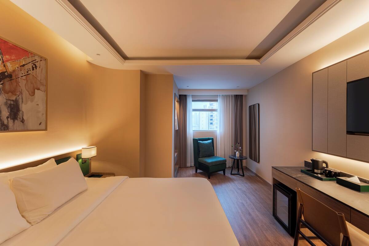 Hotellihuone, jossa on suuri sänky, työpöytä, kahvinkeitin, tuoli ja ikkunasta avautuva näkymä kaupunkiin.