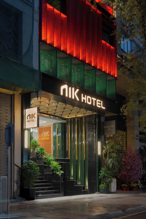 El exterior del Hotel Nik, con una fachada moderna, amplias ventanas de vidrio y una entrada destacada con escalones que conducen a la puerta.