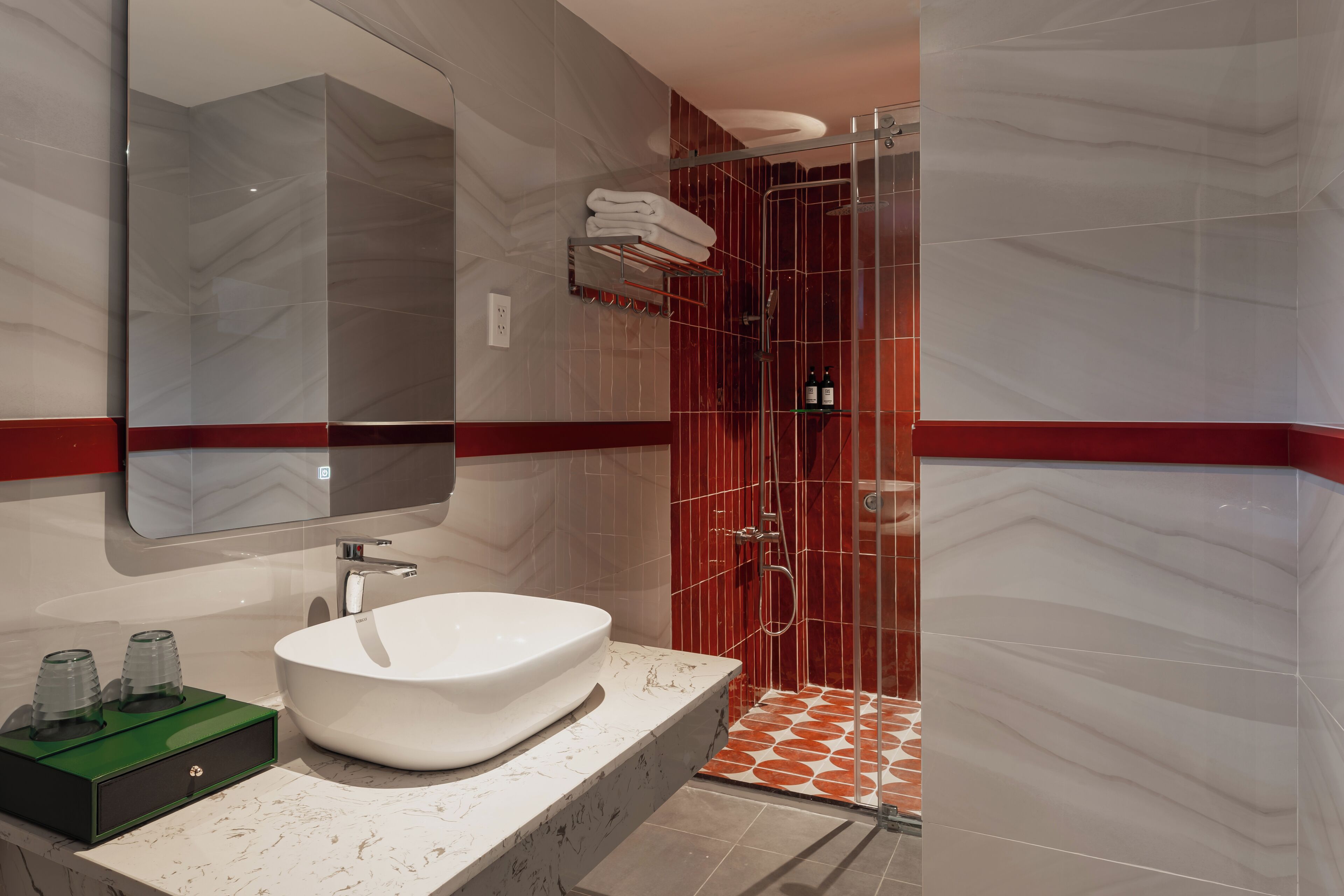 Un baño moderno con un lavamanos blanco, un espejo grande y una ducha con azulejos rojos.