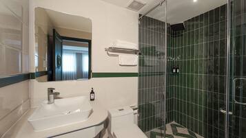 Un baño con un lavamanos blanco, un espejo, un inodoro y una zona de ducha con mampara de vidrio.