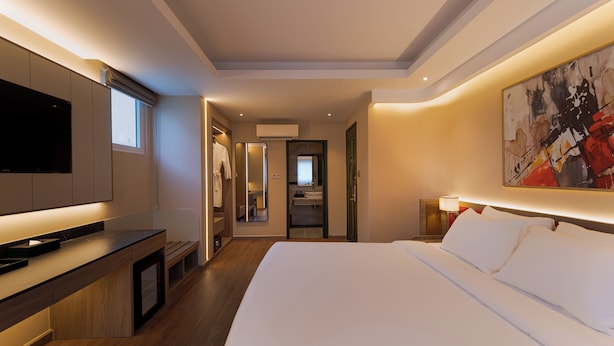 A modern hotel room with a large bed, a flat-screen TV, a desk, and a bathroom visible through an open door. - NiK Hotel Thi Sach (Ho Chi Minh City)