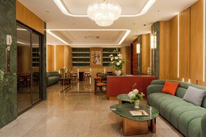 Un moderno vestíbulo de hotel con un sofá verde, una mesa redonda de centro y un mostrador de recepción.