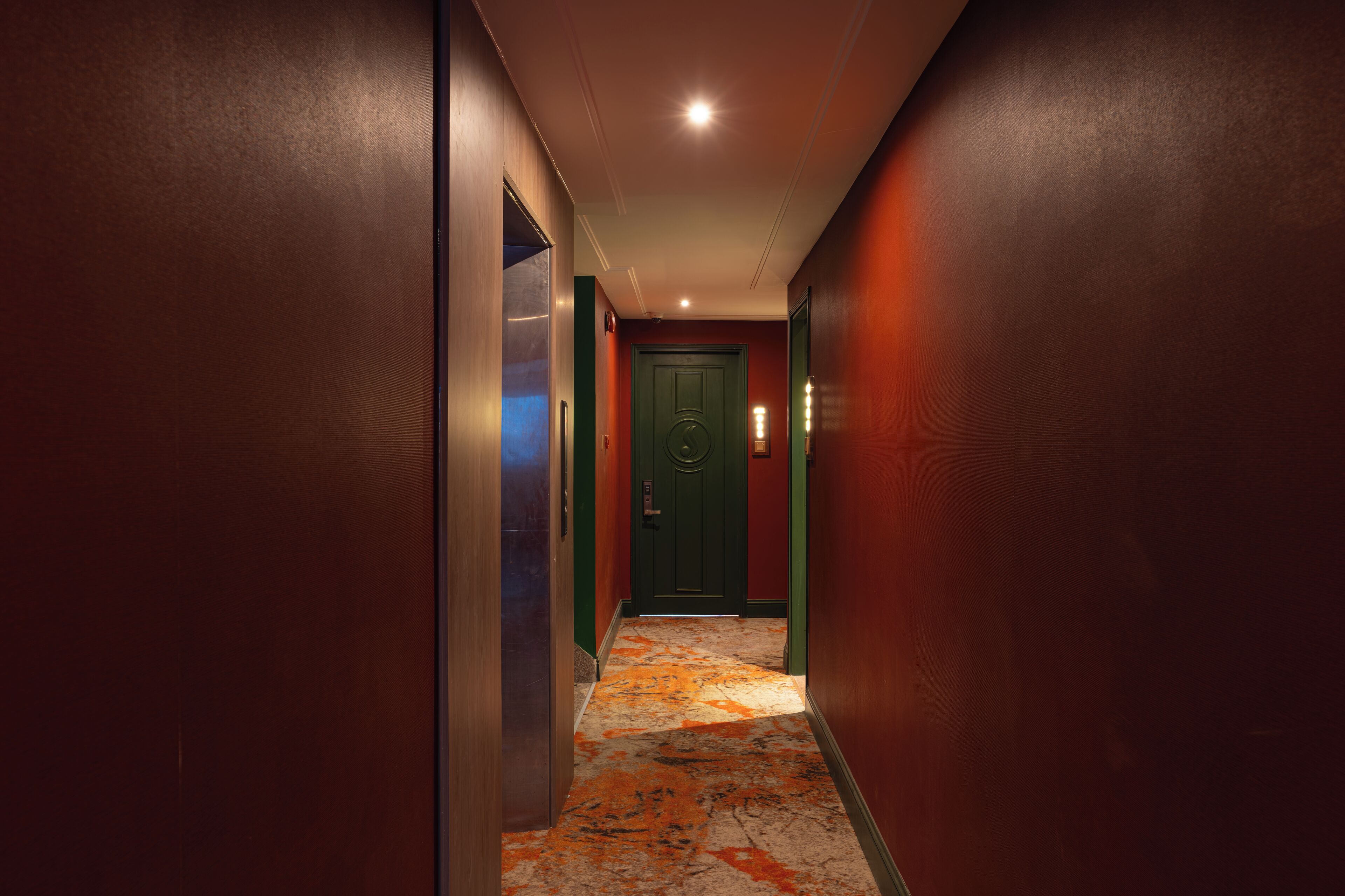 A narrow hallway with a patterned carpet, a green door, and a light fixture on the ceiling.