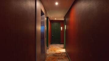 A narrow hallway with a patterned carpet, a green door, and a light fixture on the ceiling.