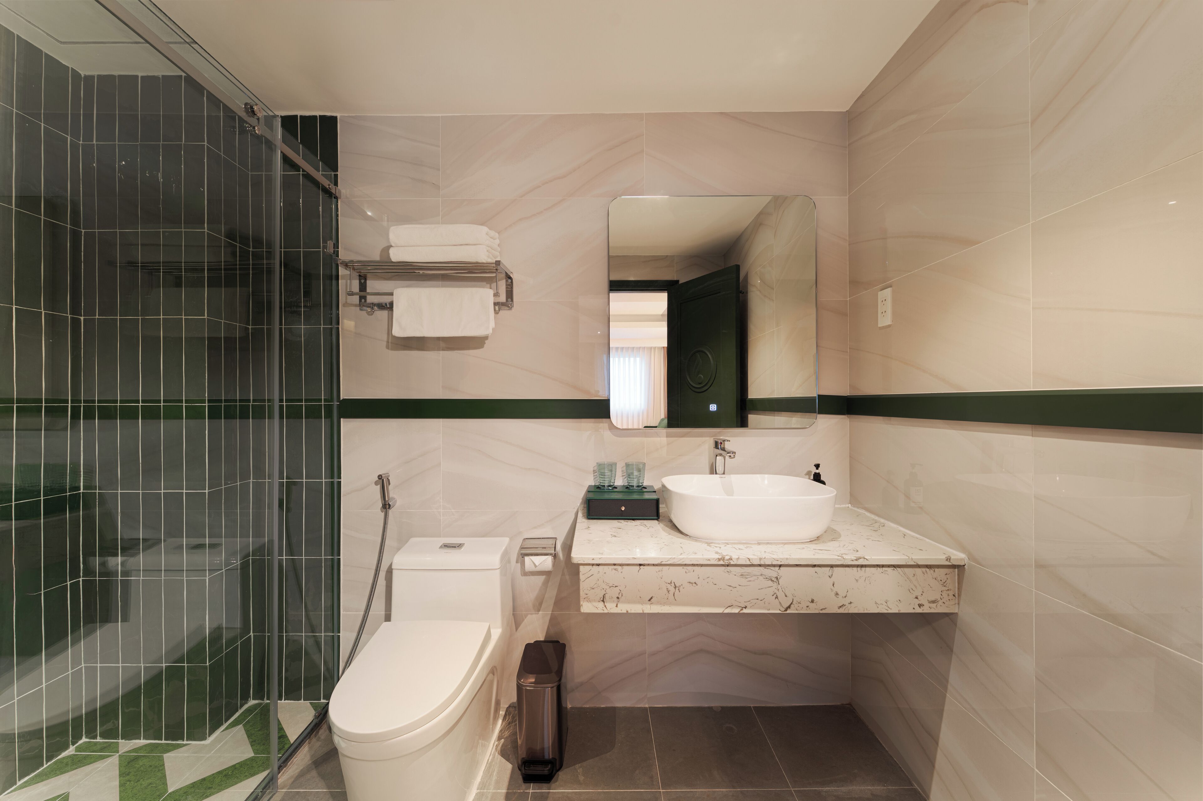 A modern bathroom with a glass shower enclosure, a white toilet, a sink with a mirror above it, and a green stripe running along the wall.