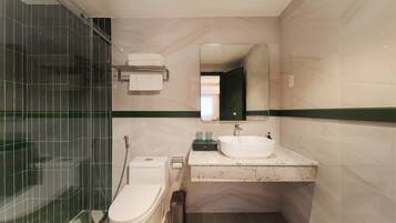 A modern bathroom with a glass shower enclosure, a white toilet, a sink with a mirror above it, and a green stripe running along the wall.