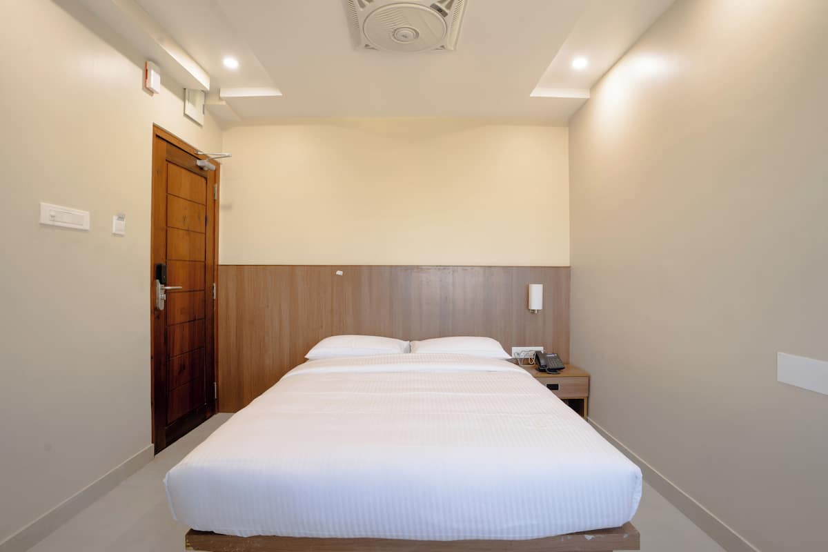 A hotel room with a single bed, a wooden headboard, a nightstand with a phone, and a door with a handle.