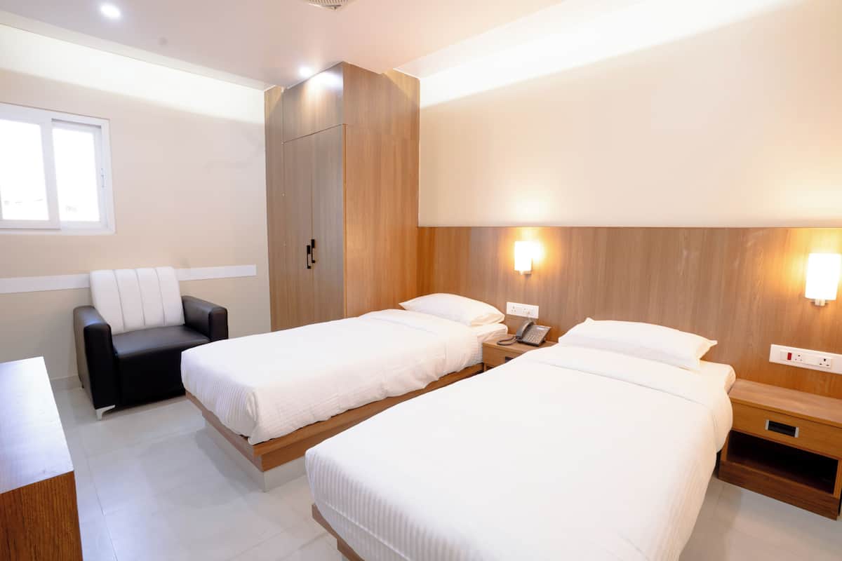 A hotel room with two beds, a desk, a chair, and a wardrobe.
