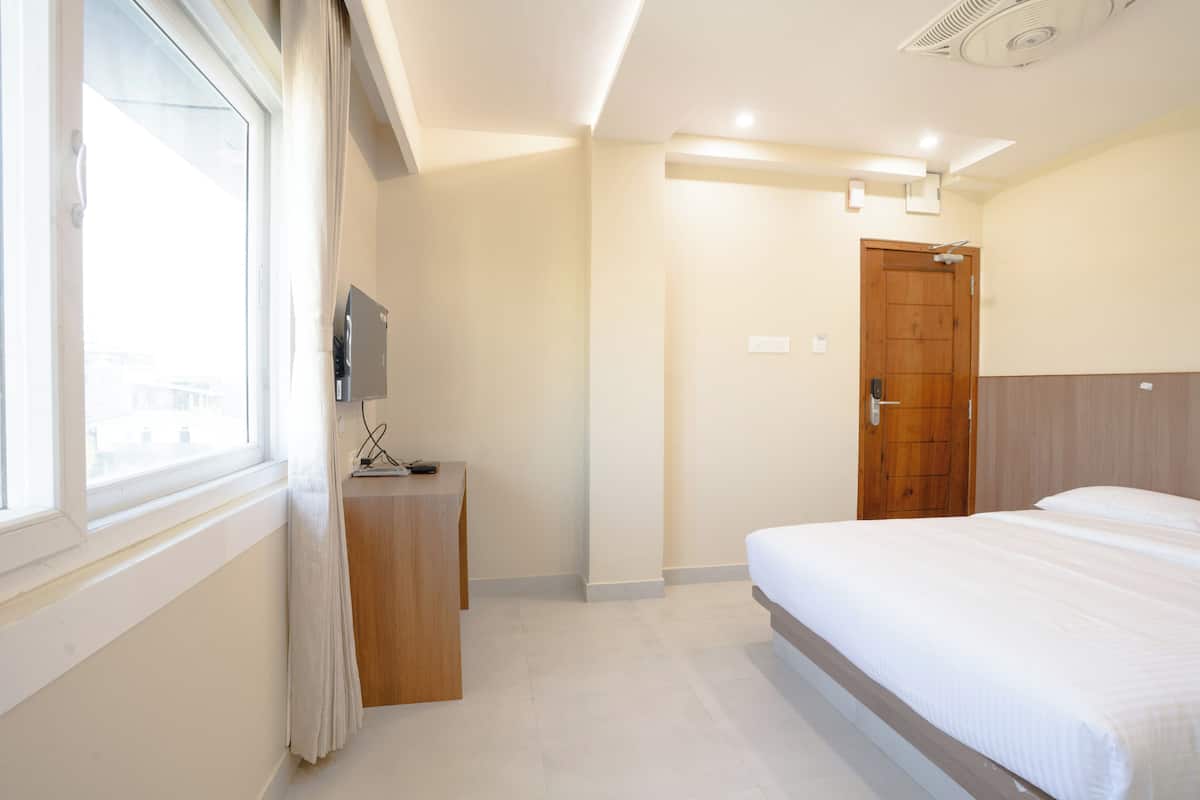 A hotel room with a bed, a desk, a TV, and a door.