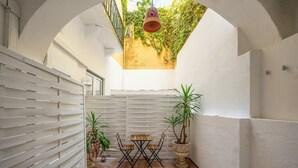 Een binnenplaats met een houten tafel en stoelen, plantenpotten en een hangende plantenbak.