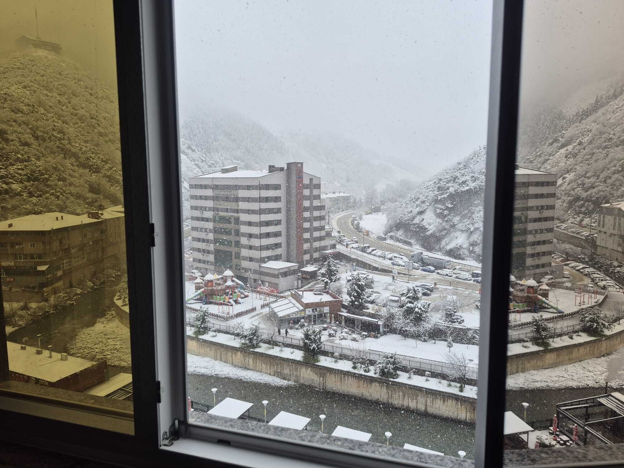 A snowy urban landscape with buildings, a playground, and a river.