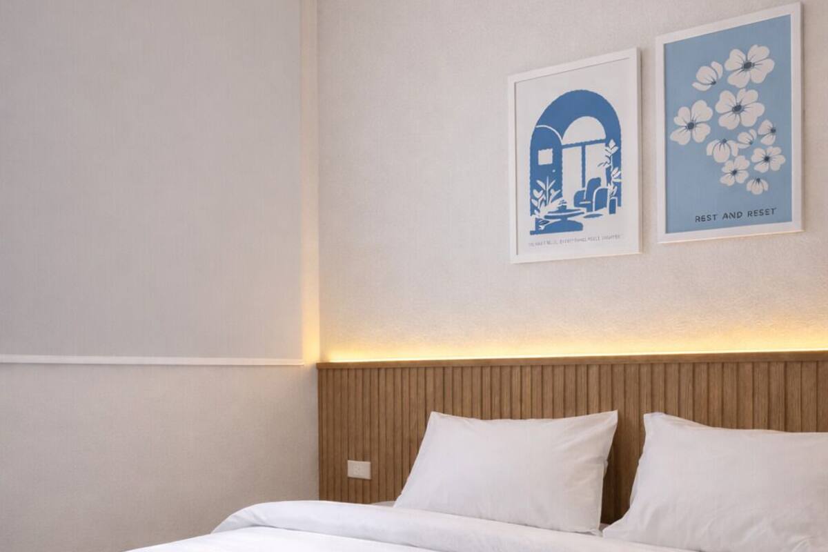 Un lit bien fait, avec du linge de lit et des serviettes blanches, une tête de lit en bois et deux œuvres d’art encadrées accrochées au mur.