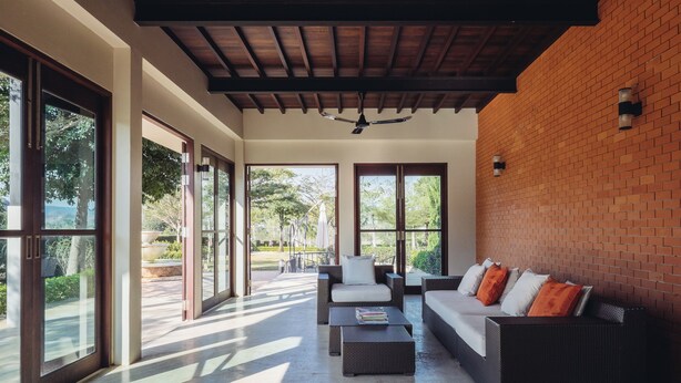Amplia zona de patio con un moderno conjunto de mobiliario exterior, grandes puertas correderas de vidrio y un muro de ladrillo.