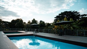 Una piscina con cubierta de baldosas, rodeada por una barandilla metálica y protegida por sombrillas.