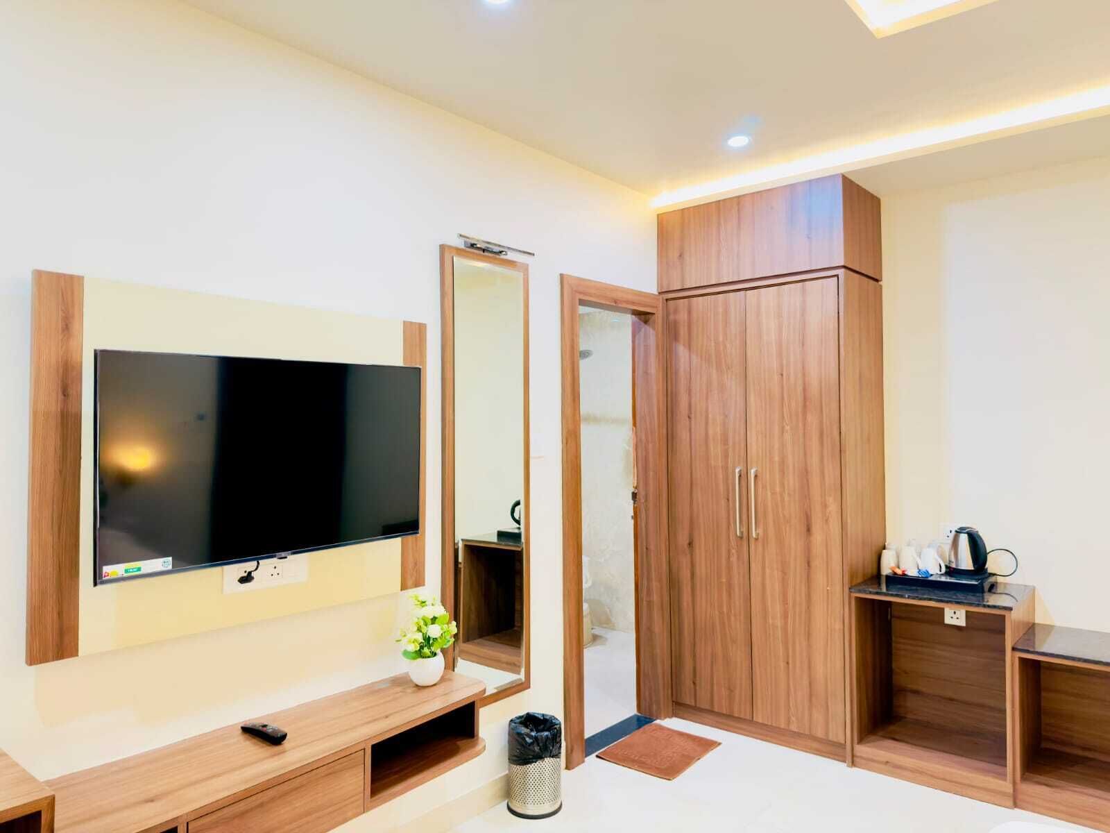 Ein modernes Hotelzimmer mit Flachbildfernseher, Holzschrank und einem kleinen Tisch mit Wasserkocher.