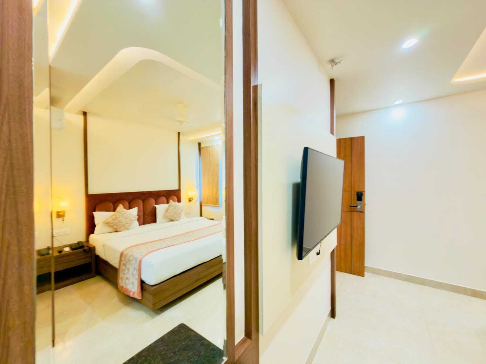 A modern hotel room with a large bed, a flat-screen TV mounted on the wall, and a wooden door.