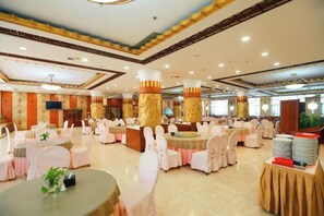 Un salón de banquetes con mesas redondas, sillas blancas y una zona de bar central.