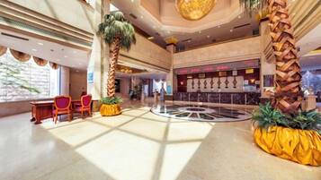 A spacious lobby with a central circular area, seating arrangements, and tall palm trees.