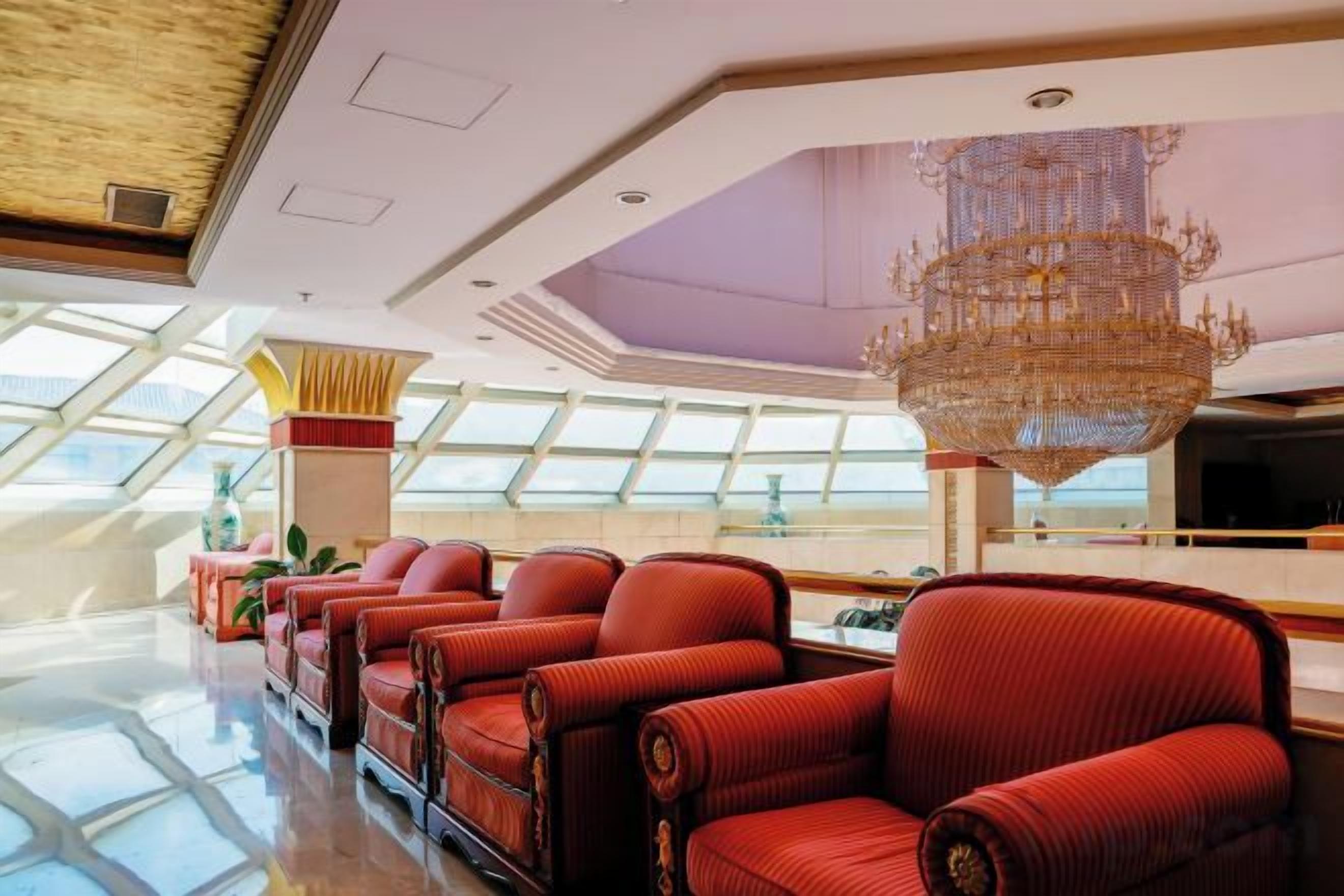 A spacious lobby with a high ceiling, a large chandelier, and a seating area with red upholstered chairs.