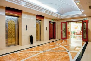 Un vestíbulo de hotel con ascensores, un basurero y un suelo de mármol pulido.