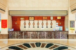 Zona de recepción de hotel con mostrador de mármol, certificados enmarcados y un letrero rojo con caracteres chinos.