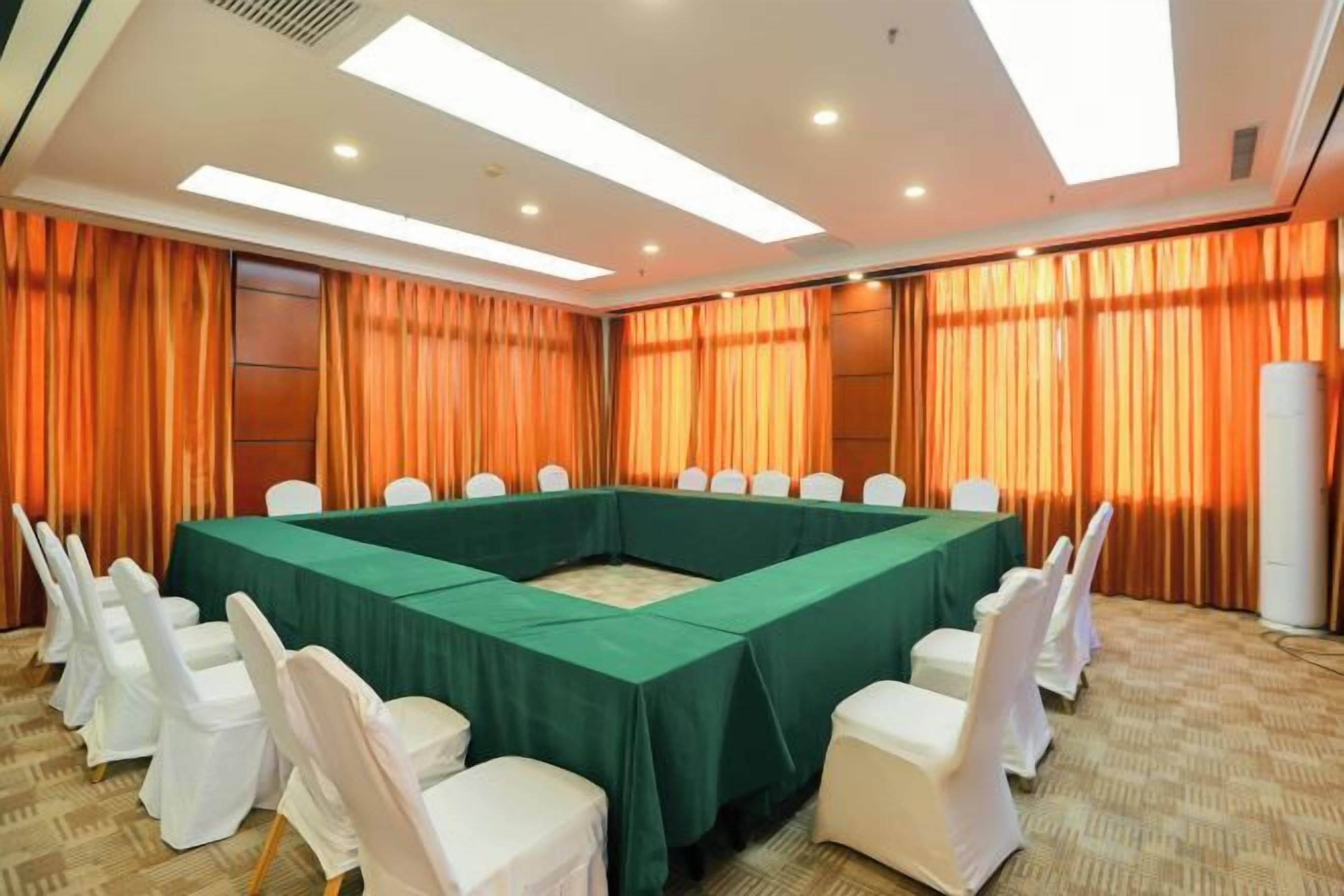 Una sala de conferencias con una larga mesa, sillas blancas y cortinas naranja.