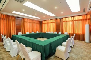 Una sala de conferencias con una larga mesa, sillas blancas y cortinas naranja.