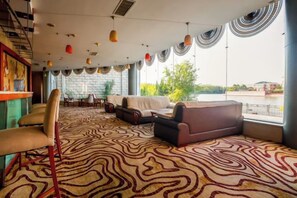 Amplia sala de estar con alfombra estampada, disposición de asientos y ventanas grandes con vistas.