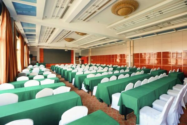 A conference room with rows of tables and chairs, a stage, and a red tiled wall. - Cangzhou Yihe Hotel (Cangzhou)