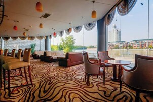 Un vestíbulo de hotel con alfombra estampada, arreglos de asientos y grandes ventanales que ofrecen vistas del paisaje urbano.