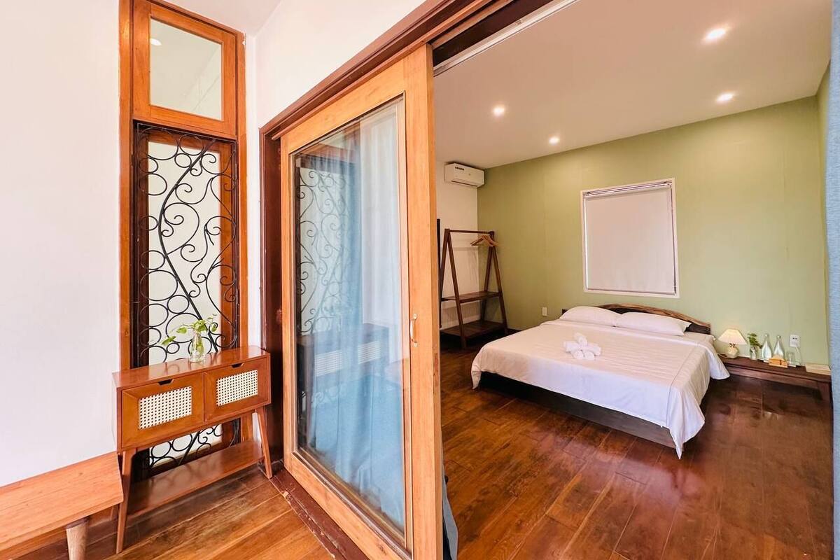 A bedroom with a bed, a wooden wardrobe, a mirror, and a sliding door.