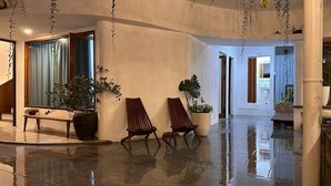 Um hall amplo com piso molhado, duas cadeiras de madeira, um banco e plantas em vasos.