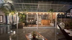 Uma área de pátio externa com balcão de madeira, assentos e plantas em vasos.