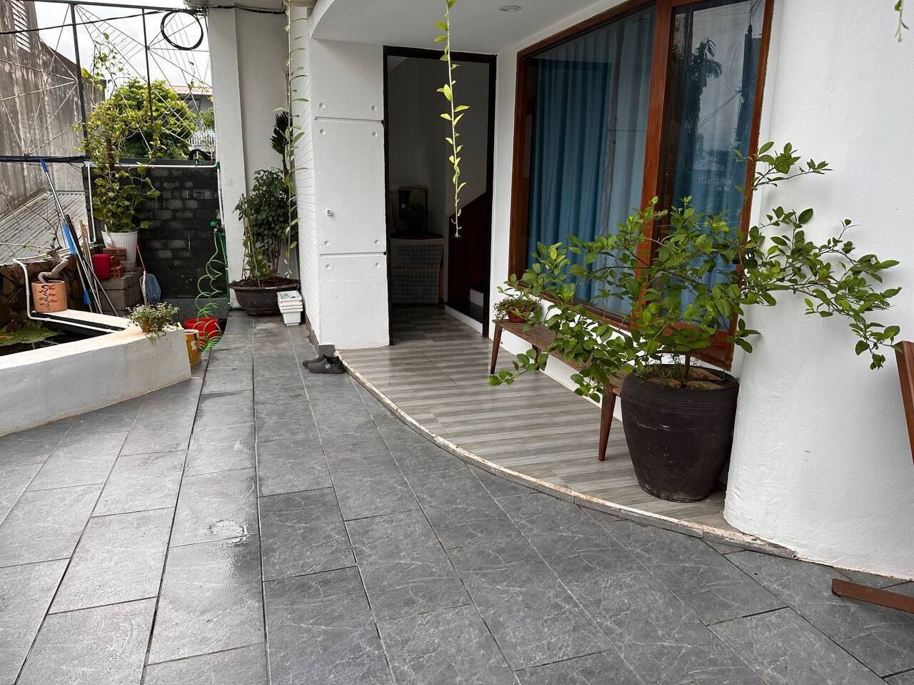 Een overdekt buitengebied met betegelde vloer, planten in potten en een houten bank.