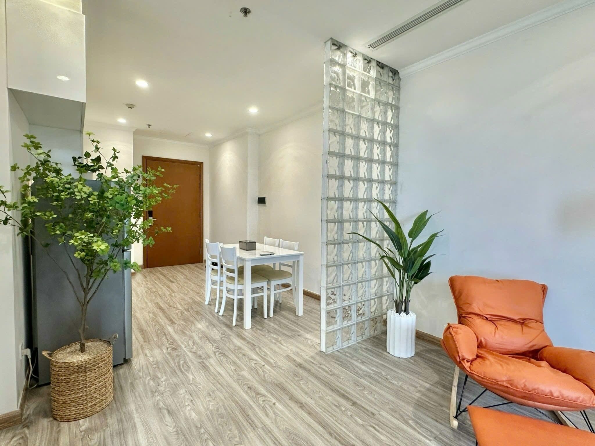 A modern room with a wooden floor, a dining table with chairs, a white partition, and a potted plant.
