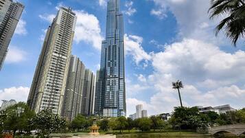 Un moderno grattacielo con facciata in vetro, circondato da un parco con uno stagno e palme.