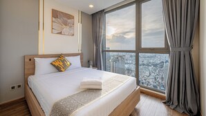 Una habitación de hotel moderna con una cama grande, vistas a la ciudad y un amplio ventanal con cortinas.