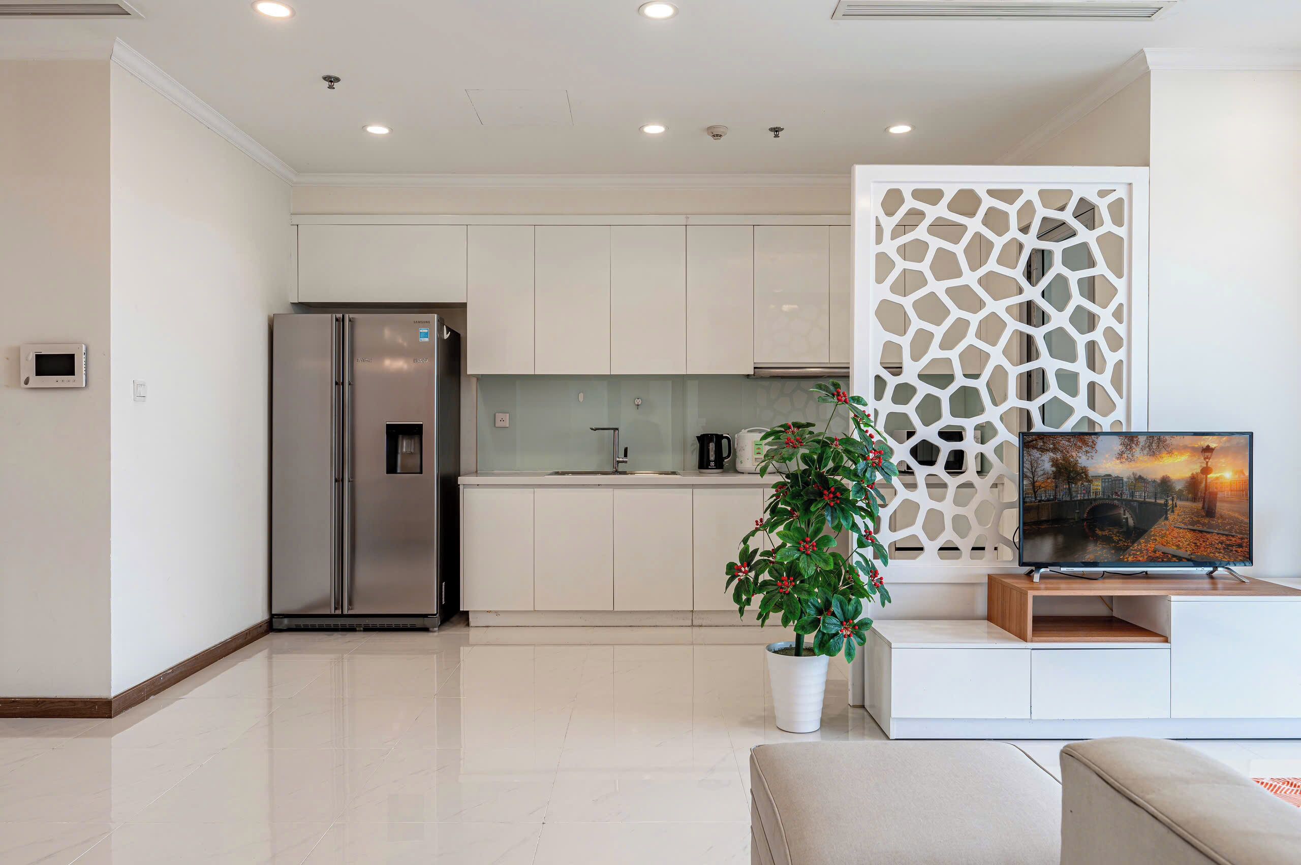 A modern kitchen with white cabinets, a stainless steel refrigerator, and a potted plant.
