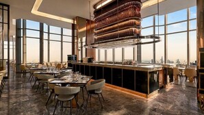 Un restaurante moderno con techo alto, ventanas amplias y una zona de bar central.