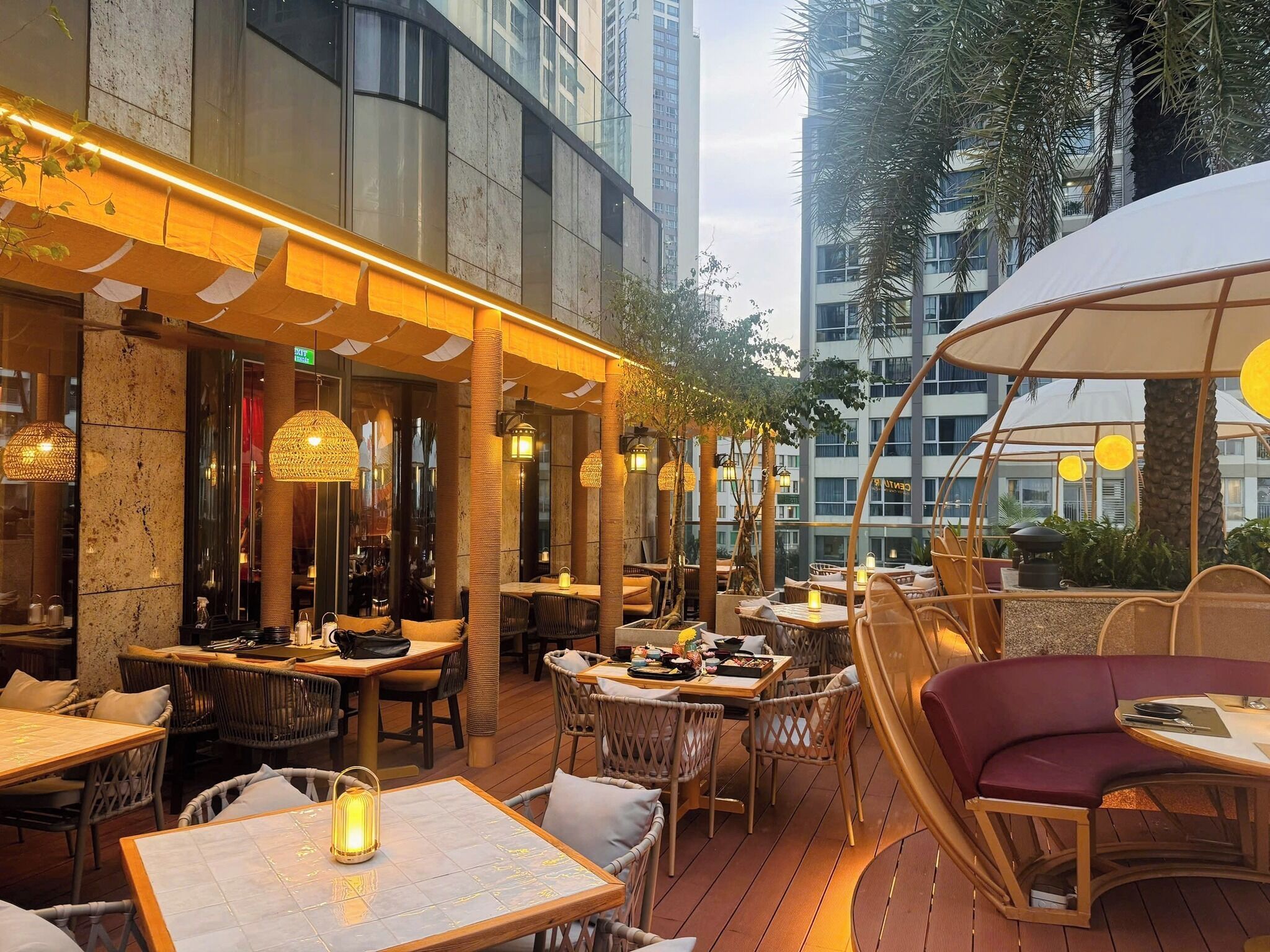An outdoor dining area with wicker furniture, tables with candles, and a view of tall buildings.